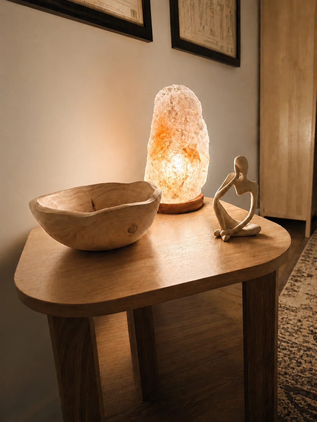 A salt lamp glowing beside a carved wooden bowl and a seated figurine on a side table.