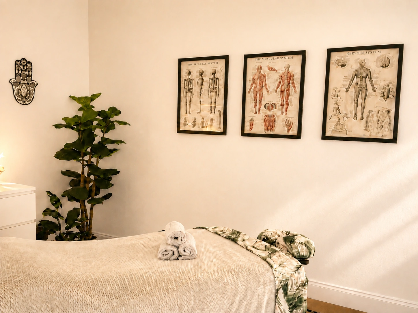 The treatment table with folded towels and anatomy charts in natural light.